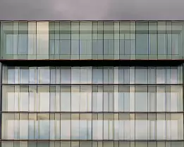Stark Modernism Tall, symmetrical glass building reflecting soft light against a backdrop of dark clouds.