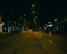 Before the City Wakes A quiet pre-dawn street in Zürich, with empty tram tracks leading into the distance under yellow streetlights and dark surrounding buildings, creating a...