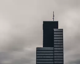 Moody Highrise Dark modern skyscraper with rooftop antenna silhouetted against an overcast sky.