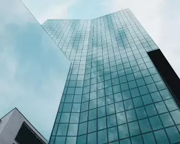 Reflective Heights Blue-tinted glass tower seen from ground level, its façade reflecting clouds and sky.