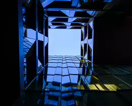 Geometric Void Looking upward through an angular glass atrium toward a square opening of clear sky.