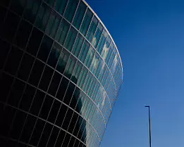 Modern Curve Rounded glass office building arcs into a bright blue sky beside a solitary lamppost.