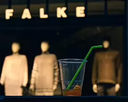 Plastic Reverie A discarded plastic cup with a green straw sits in the foreground, while three softly lit mannequins stand blurred in a fashion store window behind it.