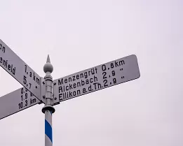Partial Directions A solitary signpost cuts into a pale winter sky, pointing outward while withholding the full picture. Distances are precise, the destination less so. The image...