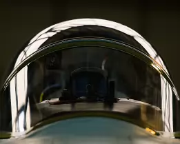 Cockpit Dome Front-facing close-up of a fighter jet canopy with hangar lights reflecting on the curved glass.