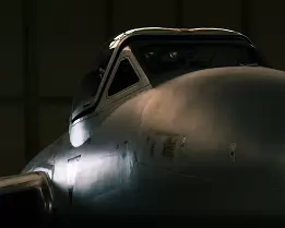 Hangar Sentinel Dimly lit side view of a vintage fighter jet’s nose and cockpit inside a hangar.