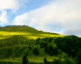 Mountain Light Rolling green hillside dappled with sunlight below a rocky mountain crest.