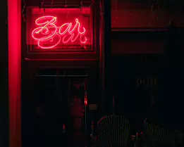 Neon Afterhours A shuttered bar glows with the last whisper of neon, its red sign spilling into empty chairs and deep shadows. A quiet moment between night and morning, where...