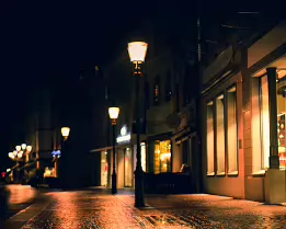After the Rain Night photograph of a wet cobblestone street glowing with warm reflections from street lamps and storefront windows, creating a quiet and atmospheric scene.