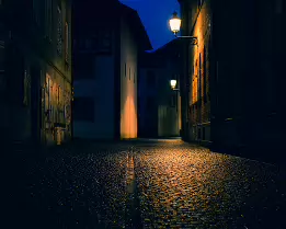 The Quiet Turn A lonely alley bends into darkness, broken only by the warm halo of distant lamps. The wet cobblestones shimmer softly, holding just enough light to suggest a...
