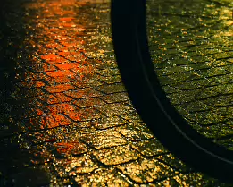 Wheel of Light The shadow of a bicycle wheel cuts through glowing cobblestones, where warm reflections shimmer like molten color. A familiar street corner becomes a painterly...