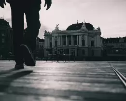 Plaza Walk Silhouetted person walks across a sunlit plaza toward a neoclassical building.